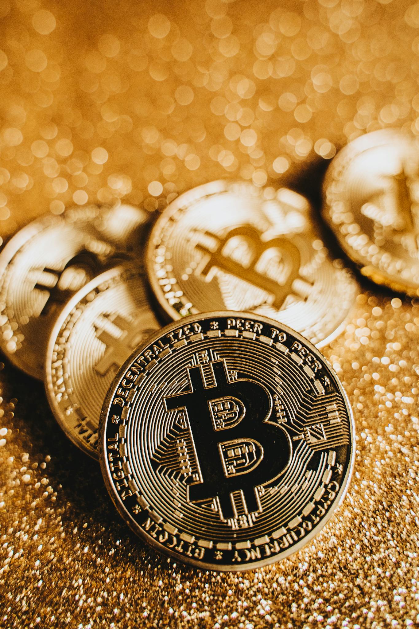 A close-up shot of shiny Bitcoin coins on a glittering gold surface, depicting digital currency and wealth.